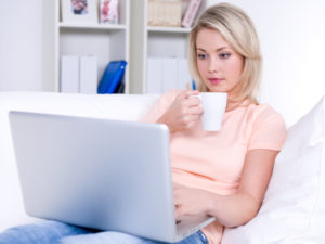 Beautiful young woman drinking coffee and using laptop
